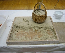 Ein viereckiger Holzrahmen und ein Korb sind mit Ton gefüllt.