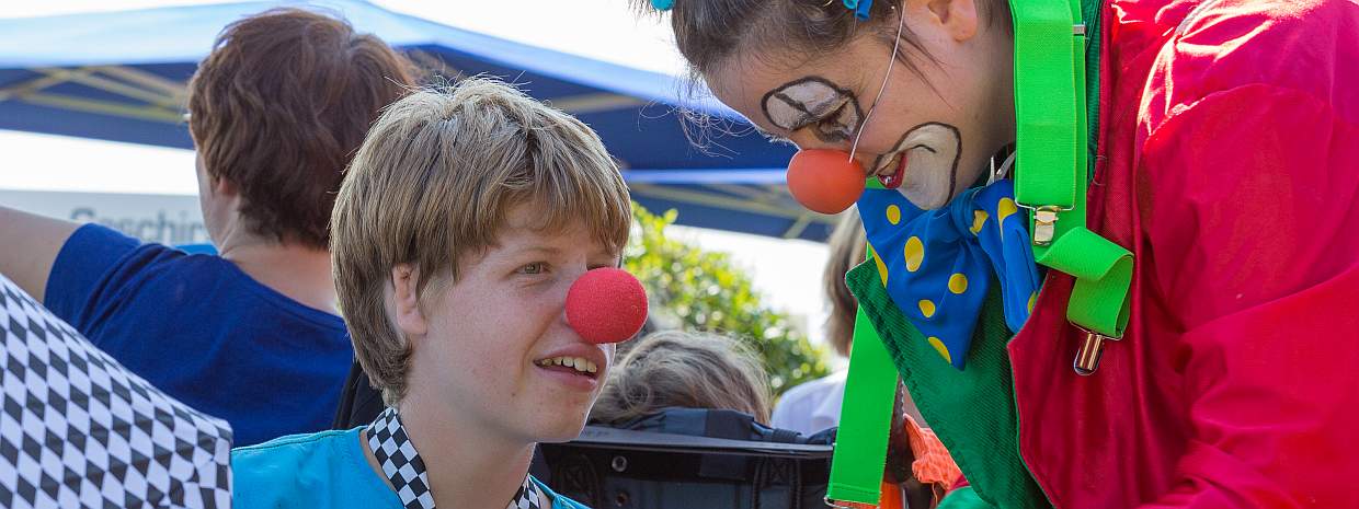 Ein Junge mit einer Clownnase unterhält sich mit einer Clownin.