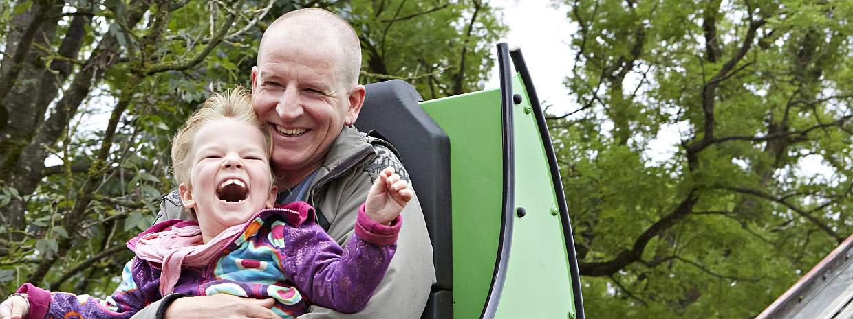 Ein Vater und seine Tochter fahren lachend auf einer Achterbahn.