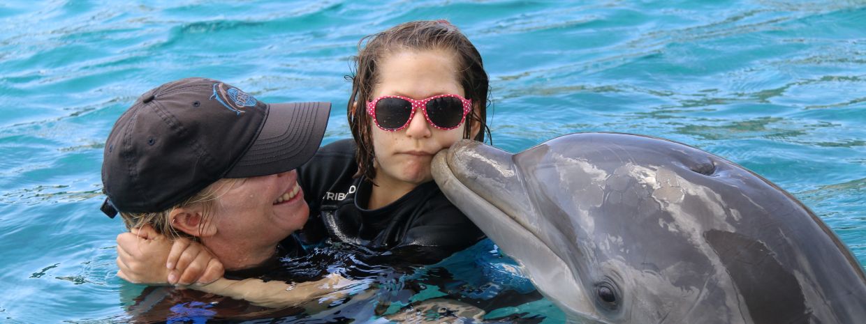 Ein Mädchen schwimmt mit Hilfe einer Trainerin mit einem Delfin.